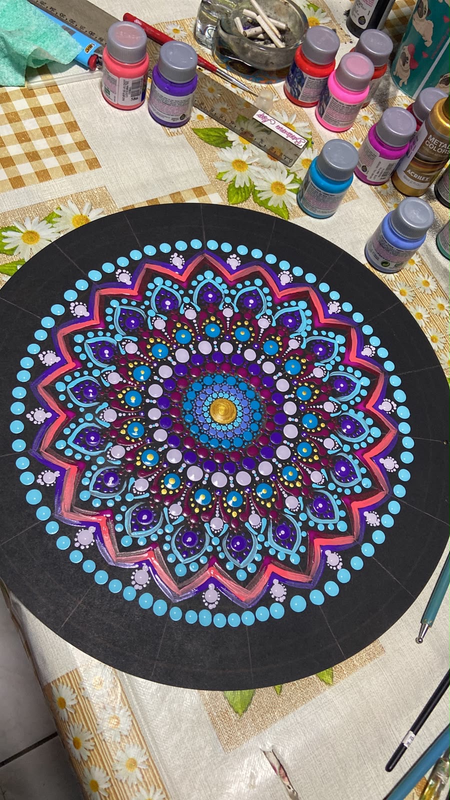 Mandala em criação sobre a mesa do ateliê, cercada de tintas